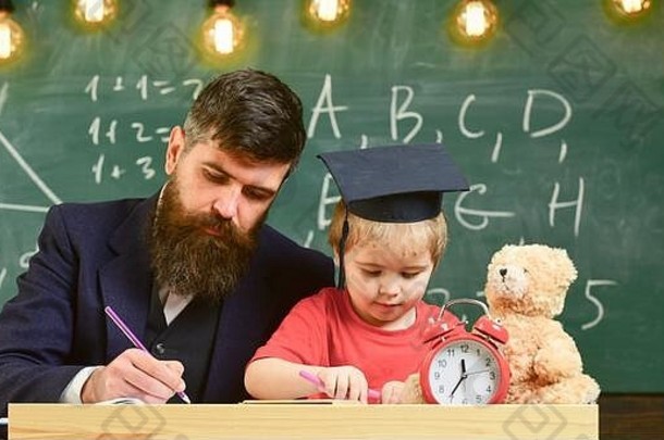 忙碌的孩子在学校学习。个人学习观念。老师穿着正式的服装，学生穿着教室里的灰泥板，背景是黑板。老师，爸爸检查作业，帮助男孩，儿子。