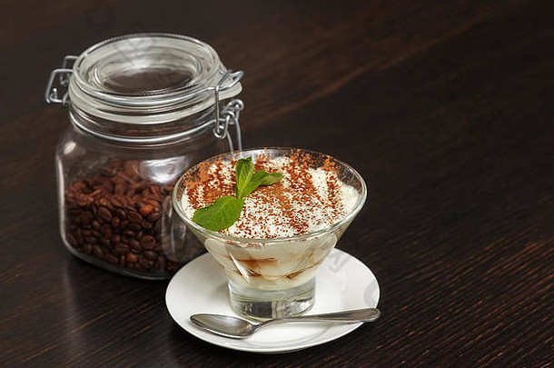 提拉米苏奶油蛋糕甜点，玻璃材质，黑色木质背景，配薄荷叶和咖啡豆