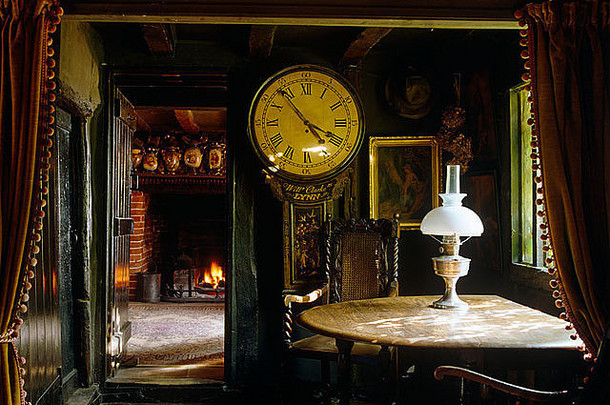 都铎别墅餐厅的古董长壳钟和带黄铜灯的旧木桌，天花板横梁较低