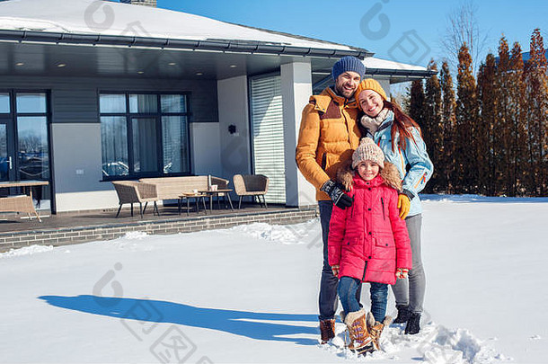 寒假。家人一起在户外站在房子附近，面带微笑，兴高采烈