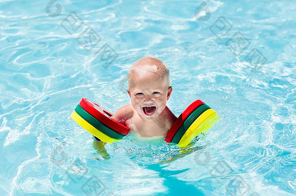 在一个炎热的<strong>夏日</strong>，快乐欢笑的小男孩在室外<strong>游泳</strong>池里玩耍。孩子们学习<strong>游泳</strong>。戴着五颜六色臂章的孩子。