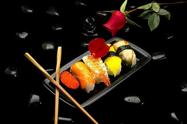 各种各样的寿司板红色的玫瑰黑色的鹅卵石黑色的背景