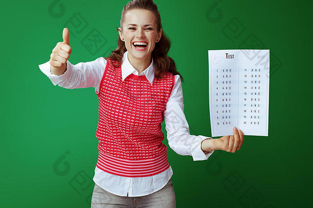 身着灰色牛仔裤和粉色无袖衬衫的年轻学生微笑着，在绿色背景下显示 考试成绩。