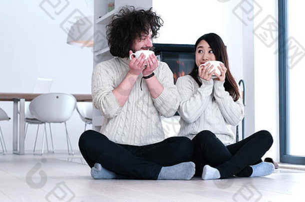 年轻的浪漫的多民族夫妇坐着地板上前面壁炉首页会说话的喝咖啡秋天一天