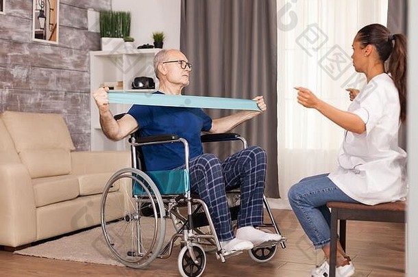 残疾老人在轮椅上接受肌肉损伤训练，治疗师使用阻力带。残障老人康复支持治疗物理治疗<strong>保健</strong>系统<strong>养老</strong>院社工