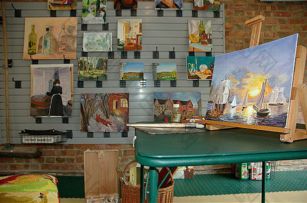 改装车库工作室绿色桌子上画架上的大型绘画，墙上展示绘画