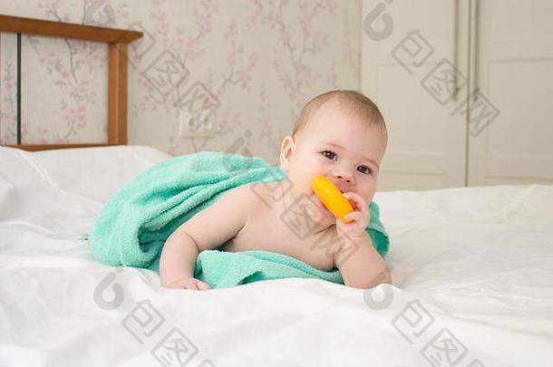 婴儿高加索女孩男孩5个月裹在毛巾里，啃着塑料百吉饼，软焦点