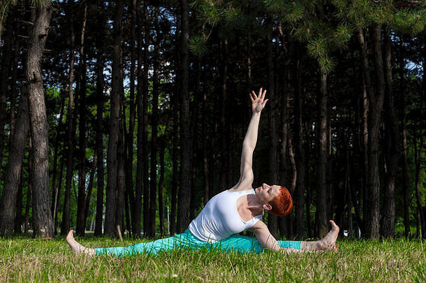 在大自然中锻炼红发女孩在公园里做瑜伽，后面是松树，阳光明媚，水平