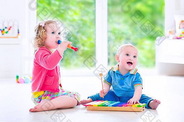 两个孩子——可爱的卷曲蹒跚学步的小女孩和有趣的小男孩，兄弟姐妹用五颜六色的木琴和长笛演奏音乐