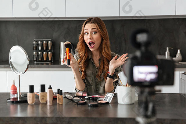 兴奋年轻的女孩记录视频博客集化妆品产品坐着厨房表格首页应用化妆