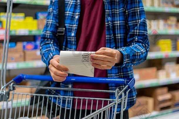 一个人的手拿着购物清单和纸张，在杂货店检查购买的产品