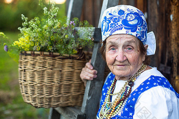 一位身着斯拉夫民族服装的老妇人在村里的房子附近，背景是一篮花。