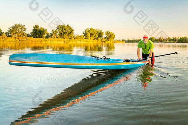 科罗拉多州北部平静的湖面上，一名男子高级桨手拿着一块直立式竞速板，欣赏着夏日的美景