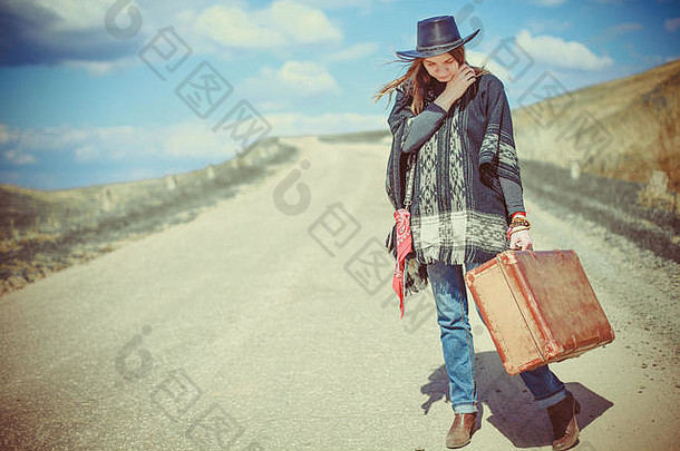 一个穿着雨披、提着手提箱的年轻女孩站在路上