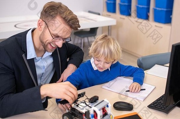 男老师和男孩坐在书桌旁，玩着可造汽车