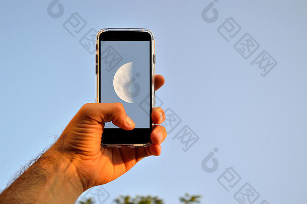 白天，人类用智能手机在蓝天上拍摄月亮的手