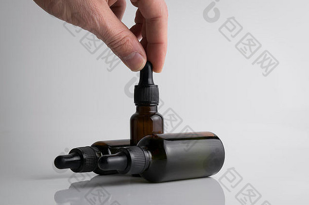 一只孤立的手，在白色背景上拿着一个医用棕色滴瓶，用于vape设备的液体瓶。