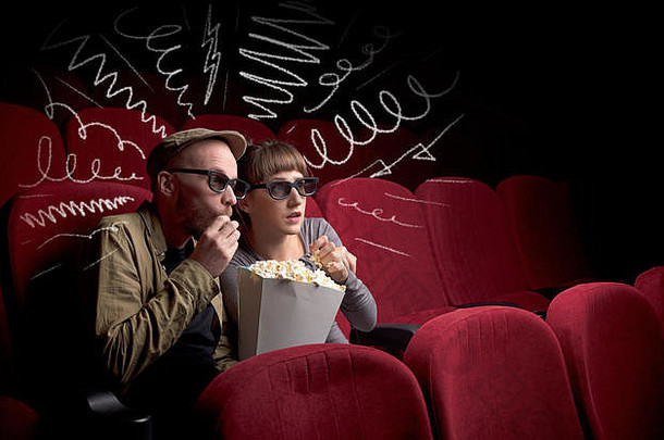 一对年轻可爱的情侣坐在电影院里，一边吃着爆米花一边看涂鸦图片的电影