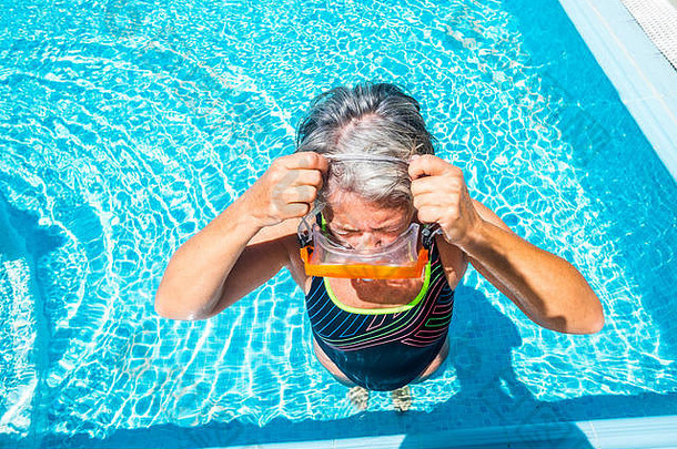 银牌协会老年活动妇女带着潜水面罩在游泳池游泳，在清澈的蓝色海水中享受夏日时光——r的健康生活方式
