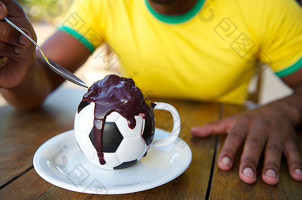 一名巴西足球运动员坐在餐馆的桌子旁，吃着<strong>足球杯</strong>里的阿卡伊