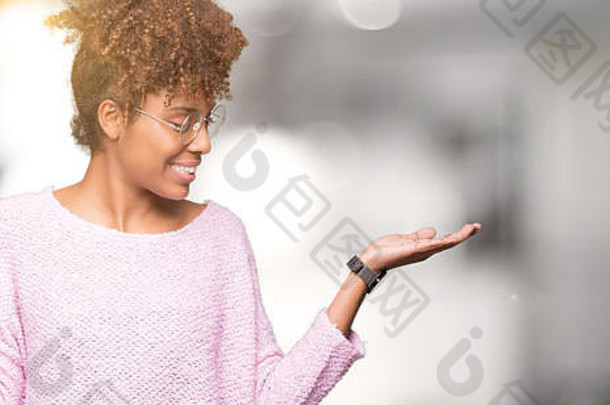 美丽的非洲裔美国年轻女子戴着眼镜，在孤立的背景下微笑着，双手张开手掌，展示和宣传公司