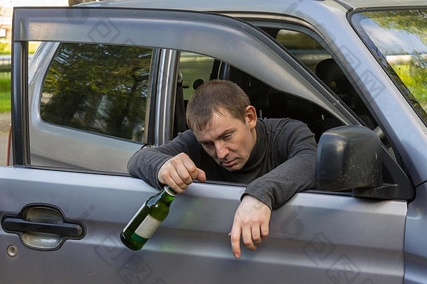 醉酒不负责任的司机拿着一瓶酒精饮料挂在车门上