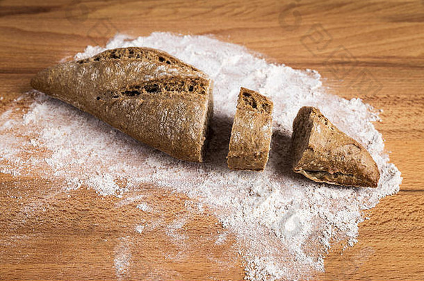 在木桌上的面粉上拉长的一小块全麦面包