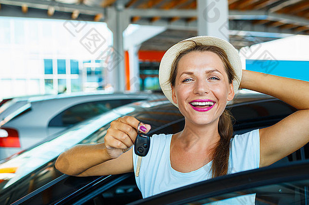 年轻快乐的女人站在车旁，手里拿着钥匙——购买二手车的概念