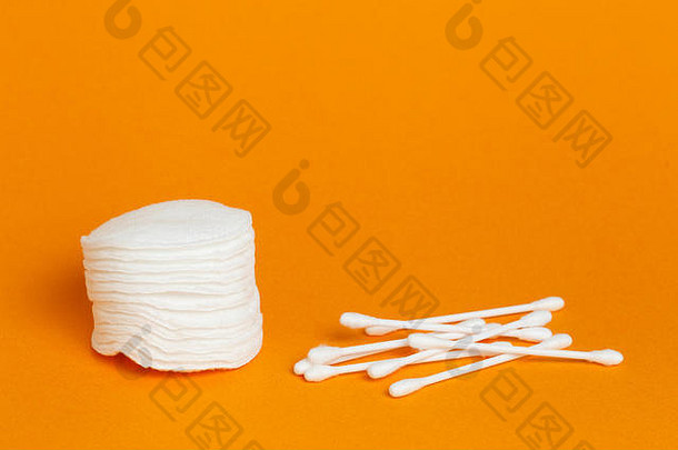 一堆白色圆形棉质海绵垫和棉签，橙色背景上留有空白