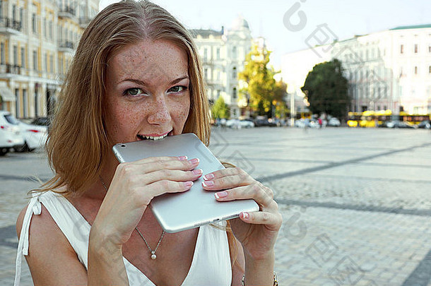 年轻的女人咬平板电脑住户外