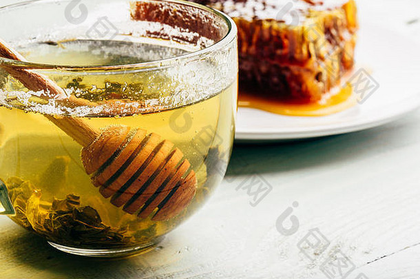 一杯绿<strong>茶</strong>中的蜂蜜勺，背景为蜂巢