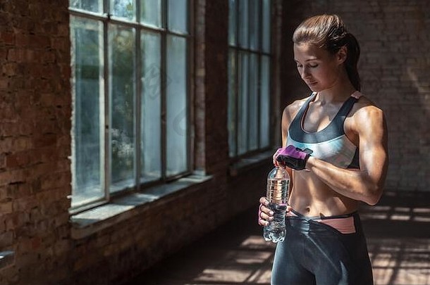 适合运动型美丽的健美女运动员穿着运动装在健身房里拿着水瓶。