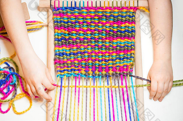 编织。在小织布机上织布的白人小女孩的手。