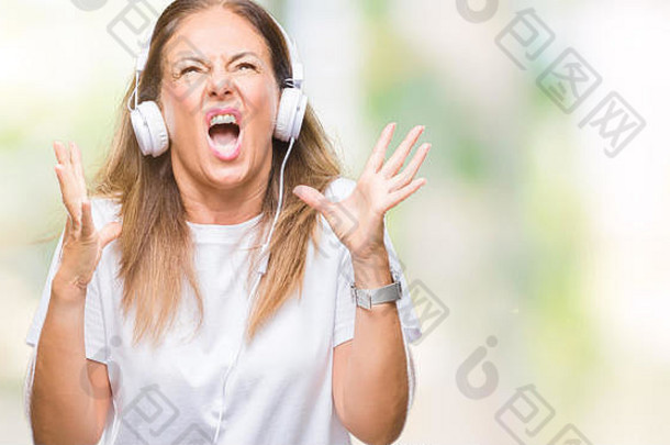 中年拉美裔妇女戴着耳机在孤立的背景下听音乐疯狂地<strong>叫</strong>喊着，表情咄咄人