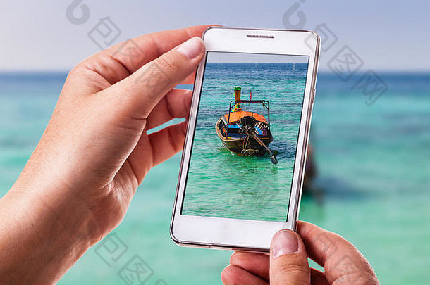 一名妇女用智能手机拍摄了一张漂浮在热带海洋中的传统泰国长尾船的照片