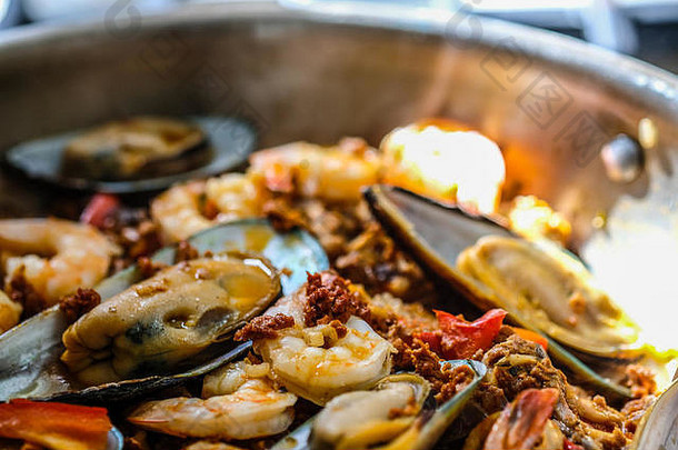 厨房炉子上的大平底锅里热气腾腾的西班牙海鲜饭的特写镜头。自然光。水平图像