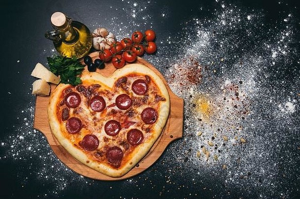 披萨心形状的意大利辣香肠西红柿马苏里拉奶酪大蒜欧芹黑色的背景