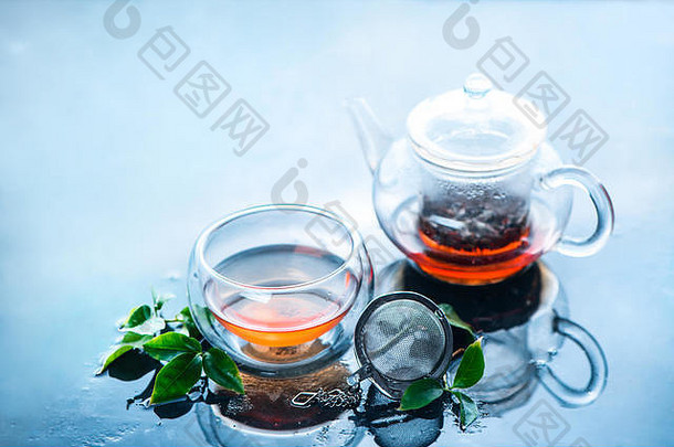 茶壶和带有茶叶的双壁玻璃，浅蓝色背景上清晰而清新的图像。有复印空间的热饮。