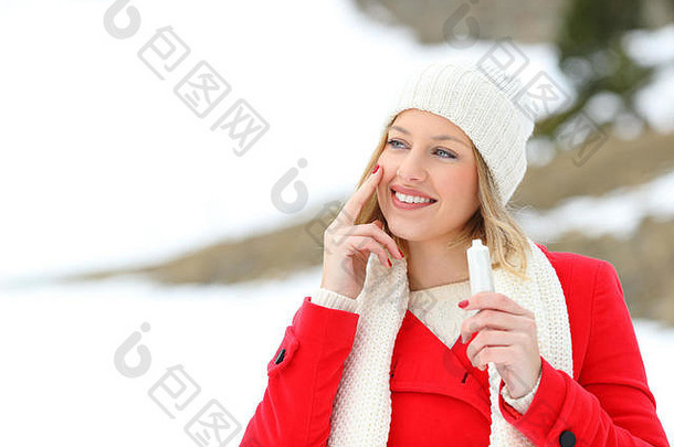一位穿着红色保护皮肤的时尚女孩的肖像画，在冬天的雪山上涂抹保湿霜