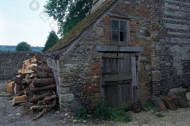 一个破旧的谷仓的外部，墙上靠着一堆圆木