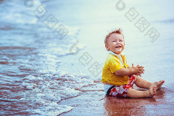 孩子男孩黄色的衬衫红色的短裤坐着海滩关闭水玩笑微笑