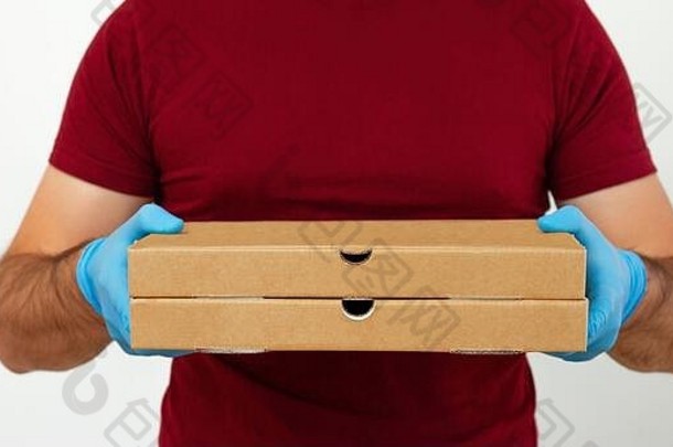 一个带着医用手套和红色t恤的快递员拿着比萨饼<strong>盒</strong>。在检疫期间运送比萨饼。非接触式递送
