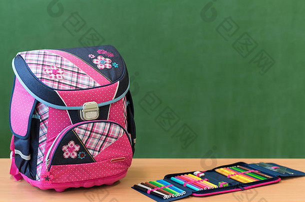 靠着绿板的书桌上放着粉红色的少女装书包和铅笔盒。开学第一天的概念。