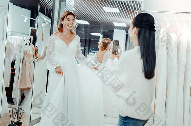美丽的新娘和她的伴娘正在为一件礼服拍照。