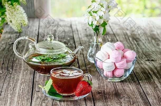 美丽的构图，一杯茶和棉花糖放在自然背景的木制野餐桌上。在乡下度假的概念。