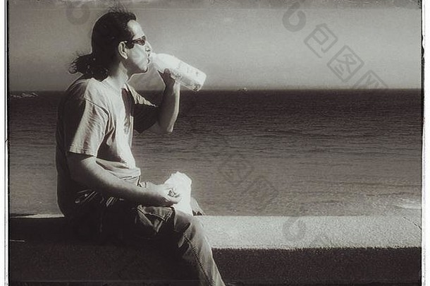 在一个美丽的日子里，坐在墙上喝牛奶的男人