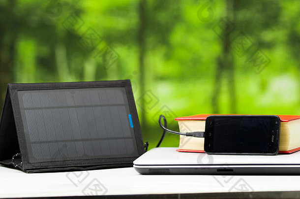 便携式太阳能充电器在白色桌面上，与平板电脑相连，现代科技理念，窗户花园背景