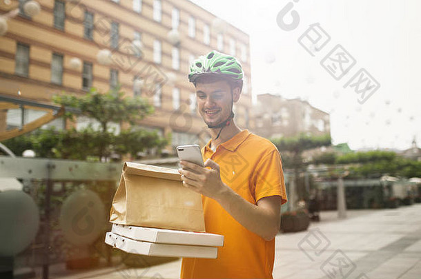 一个穿着黄衬衫的年轻人用小玩意跟踪城市街道上的订单，运送比萨饼。使用在线应用程序接收和跟踪发货地址的快递员。现代技术。