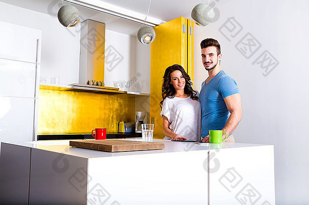 一对年轻夫妇一边在厨房里使用平板电脑一边喝咖啡。