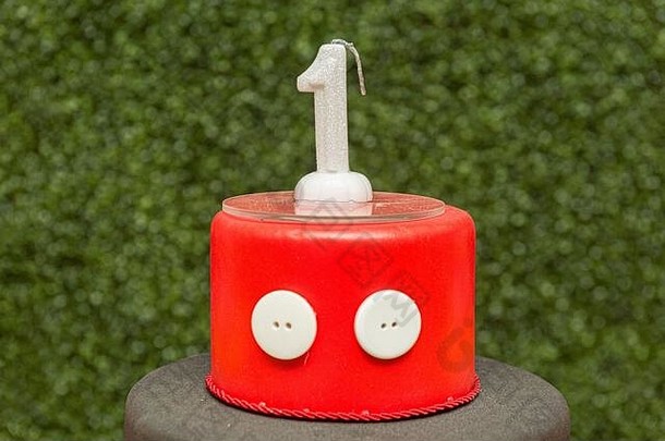 红色假蛋糕的顶部有一个形状模糊的绿色背景蜡烛。白色的一周年庆祝活动。儿童生日晚会